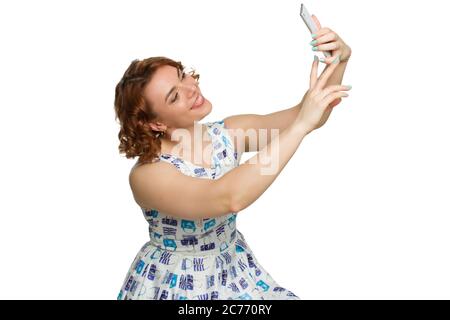 Portrait d'une jeune fille en surpoids à tête rouge sur un fond blanc isolé, photographié en profil, se berner et prendre un selfie Banque D'Images