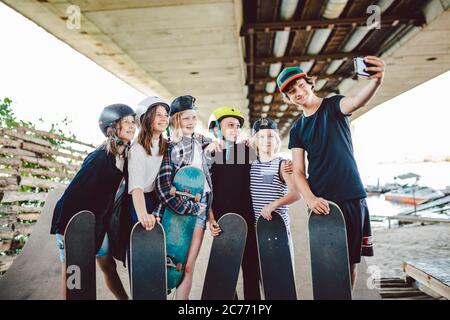 groupe d'enfants de skateboarders font du contenu de médias sociaux sur téléphone tout en passant du temps sur la rampe dans le parc de skate. Amis se tiennent ensemble avec des planches de skate Banque D'Images