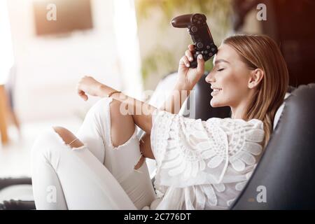 Femme souriante jouant à des jeux vidéo à la maison, avec joystick Banque D'Images