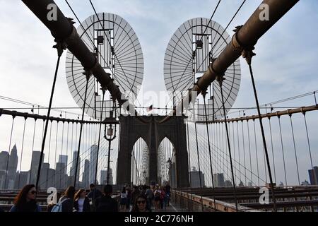 Une barrière circulaire / disque sur les câbles en direction de la tour du pont de Brooklyn, New York. Des piétons traversent le pont sous les câbles. Banque D'Images