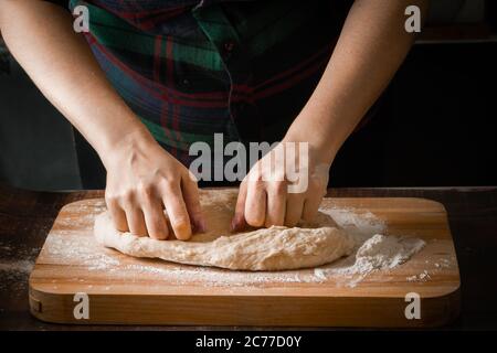 Gros plan des mains du cuisinier. Une femme prépare de la pâte à pétrir sur une planche à farine Banque D'Images