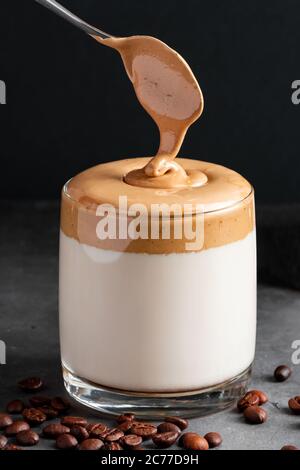 Café Dalgona sur fond noir. Le processus de fabrication d'une boisson tendance. Mousse douce et moelleuse dans un verre avec du lait glacé. Photo verticale Banque D'Images