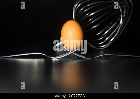 Œuf frais bio debout sur deux fourchettes jointes sur fond noir Banque D'Images