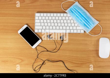 Clavier, souris, smartphone, casque et masque sur table en bois avec espace pour le texte ou le design. Banque D'Images