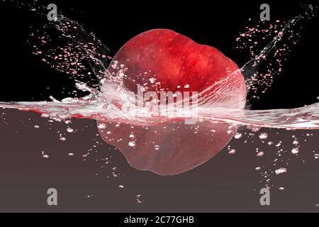 Pomme rouge tombant dans l'eau avec les éclaboussures isolat sur fond noir. Banque D'Images