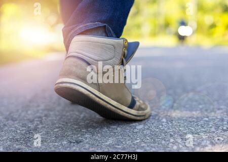 Homme en jeans et baskets de sport marchant sur la route. Concentrez-vous sur les baskets. Effet de lumière du soleil. Avec espace de copie pour le texte ou la désie Banque D'Images