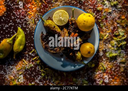 Gros plan de Bharela Marcha classique ou de piments frits farcis dans une assiette en verre avec des citrons et toutes les épices nécessaires pour la préparer sur une br Banque D'Images