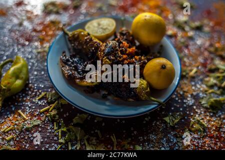 Gros plan de Bharela Marcha classique ou de piments frits farcis dans une assiette en verre avec des citrons et toutes les épices nécessaires pour la préparer sur une br Banque D'Images