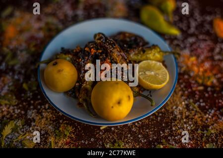 Gros plan de Bharela Marcha classique ou de piments frits farcis dans une assiette en verre avec des citrons et toutes les épices nécessaires pour la préparer sur une br Banque D'Images