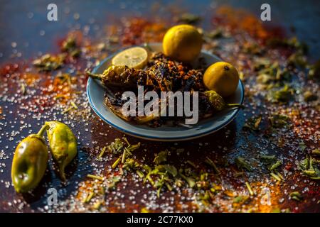 Gros plan de Bharela Marcha classique ou de piments frits farcis dans une assiette en verre avec des citrons et toutes les épices nécessaires pour la préparer sur une br Banque D'Images