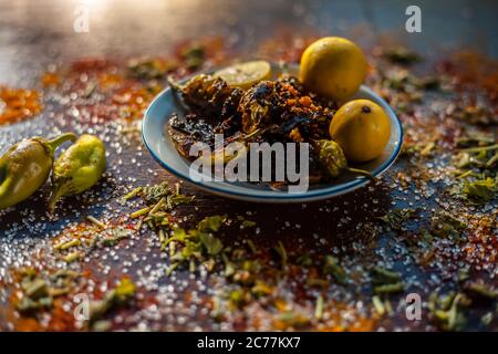 Gros plan de Bharela Marcha classique ou de piments frits farcis dans une assiette en verre avec des citrons et toutes les épices nécessaires pour la préparer sur une br Banque D'Images