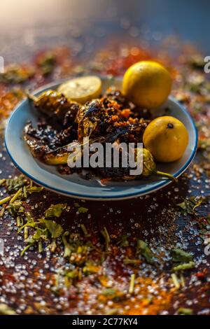 Gros plan de Bharela Marcha classique ou de piments frits farcis dans une assiette en verre avec des citrons et toutes les épices nécessaires pour la préparer sur une br Banque D'Images