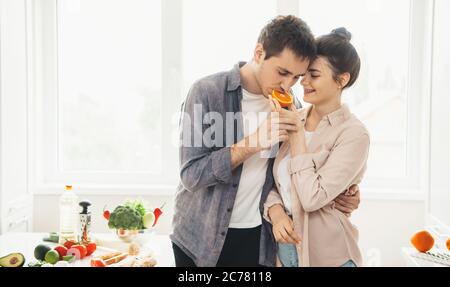 Les jeunes couples caucasiens qui ont des habitudes saines s'embrassent et mangent de l'orange dans la cuisine Banque D'Images