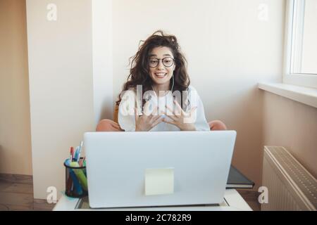 Jeune étudiant aux cheveux maussants lors de cours en ligne portant des lunettes et des écouteurs exprimant devant l'ordinateur portable Banque D'Images