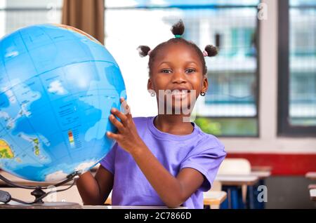Scène de l'école élémentaire. Une écolière africaine utilisant le monde entier dans la salle de classe. Banque D'Images