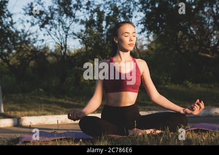La fille est assise avec les yeux fermés dans une position de lotus. Banque D'Images