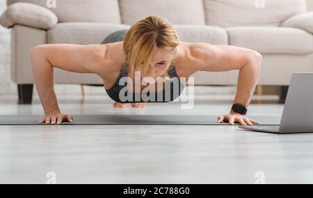 Des poups à la maison. Femme adulte faisant des exercices de fitness sur tapis de sol avec ordinateur portable Banque D'Images