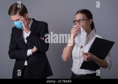 Portrait de deux jeunes hommes d'affaires en vêtements d'affaires. Le mec masqué couvre son visage avec sa main, craignant une infection par une fille malade qui éternue Banque D'Images