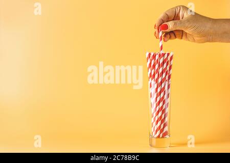 Femme cueillette main de paille de papier. Pailles écologiques jetables en papier coloré pour les cocktails d'été dans une tasse de verre sur fond jaune avec CO Banque D'Images