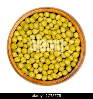 Pois verts en conserve dans un bol en bois. Petites graines sphériques de la gousse de fruits Pisum sativum, bouillies et en conserve pour préserver les légumineuses. Gros plan par le dessus. Banque D'Images