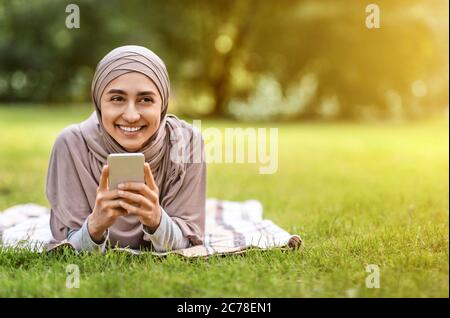 Rire une femme musulmane en utilisant son smartphone, se reposant dans le parc Banque D'Images