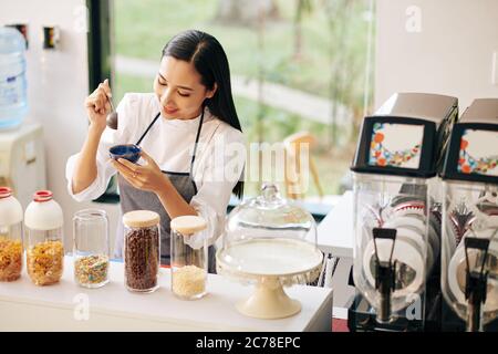 Jolie jeune femme vietnamienne souriante décorant de la glace dans un petit bol avec des saupoudrées Banque D'Images