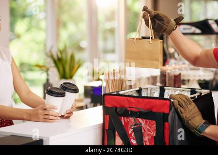 Image rognée d'un coursier mettant du yaourt frais non laitier et des tasses de café à emporter dans un sac pour livrer la commande au café local Banque D'Images