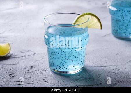 Délicieux cocktail de couleur bleue avec des graines de basilic chia et une tranche de citron vert dans deux verres, boisson d'été saine, fond en béton de pierre Banque D'Images