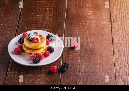 Crêpes au fromage cottage et sucre en poudre, beignets de caillé dessert aux framboises et aux mûres dans un plat sur fond de bois brun foncé Banque D'Images