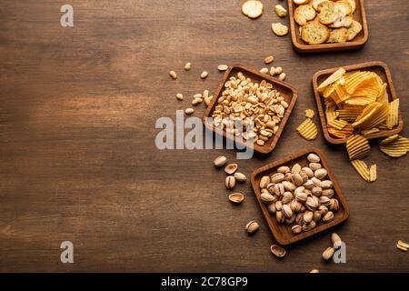 Encas croustillants sur fond. Pistaches, noix, chips et chips dans un plat et dispersés sur une table Banque D'Images