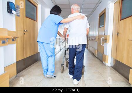 Infirmière asiatique aidant un homme âgé avec un marcheur marchant à l'étage de l'hôpital, vue arrière. Banque D'Images