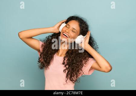 Une jeune fille afro-américaine vivace qui apprécie sa musique en écoutant une bande son sur un casque stéréo avec un sourire éclatant de plaisir, portrait de studio Banque D'Images