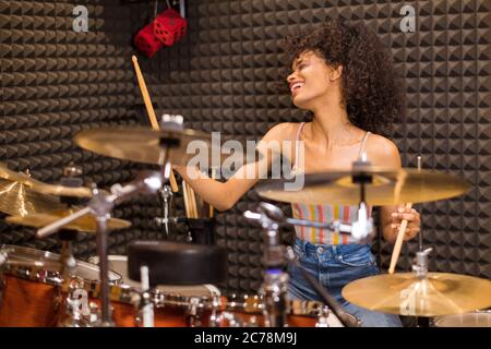 Jeune femme noire batteur dans un studio d'enregistrement immergé dans le plaisir de sa musique jouant un ensemble de batterie et de cymbales Banque D'Images