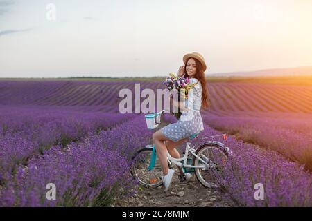 jolie femme brune qui s'éloigne dans le champ de lavande. femme en robe et chapeau de paille qui s'amuse dans les fleurs de lavande Banque D'Images