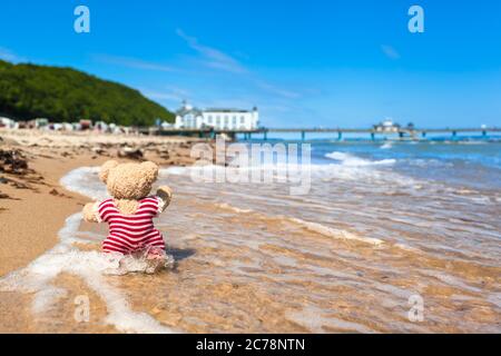 Ours en peluche en maillot de bain rayé nostalgique Profitez de la vie de plage en mer près du bâtiment de la jetée (espace copie) Banque D'Images