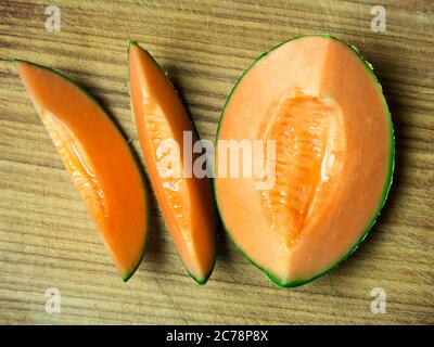 Deux tranches de melon de canteloup et un quart de melon sur une planche à découper en bois Banque D'Images