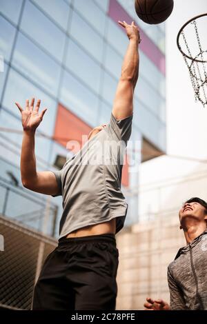 deux jeunes hommes adultes asiatiques jouant au basketball en tête-à-tête sur un terrain extérieur Banque D'Images