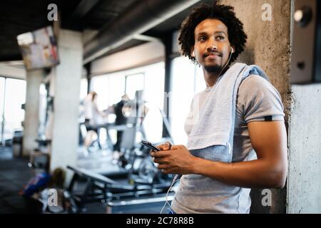 Jeune homme musclé à l'aide de téléphone mobile à la salle de sport dans l'exercice rompre Banque D'Images