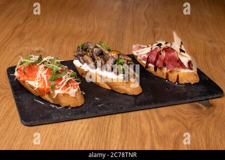 Trois délicieux bruschettas juteux de pain aux champignons, au bacon, au fromage et aux tomates sur un support en marbre noir. En-cas avec du pain au restaurant. Banque D'Images