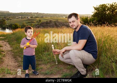 Papa et son fils jouent des bulles de savon dans la nature dans un champ jaune d'été. Pendre avec son père, la paternité et l'enfance. Banque D'Images