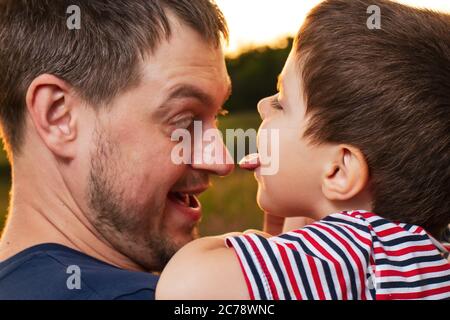 Le fils lèche la langue de son père dans le nez. Jeux d'enfant et d'adulte, amour, fête des pères. Papa et bébé jouent sur le terrain. Banque D'Images