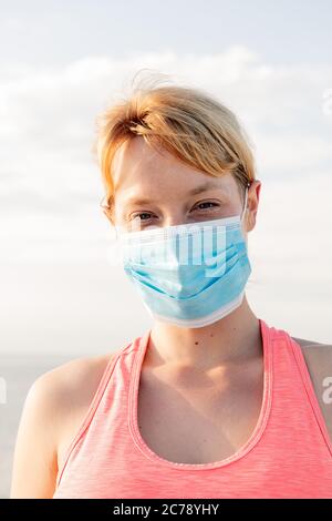 portrait vertical d'une belle femme blonde avec un masque protecteur avec le ciel en arrière-plan, concept de prévention et de soins de santé Banque D'Images