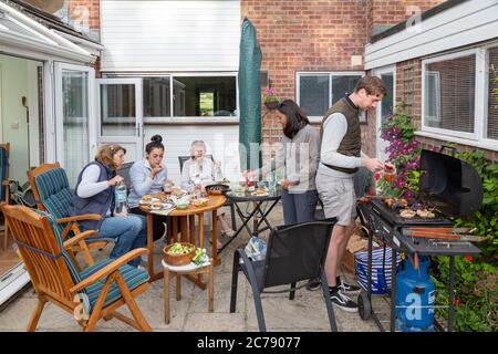 Une famille de trois générations ayant un barbecue familial à la maison dans le jardin arrière, Oxfordshire Angleterre Royaume-Uni Banque D'Images