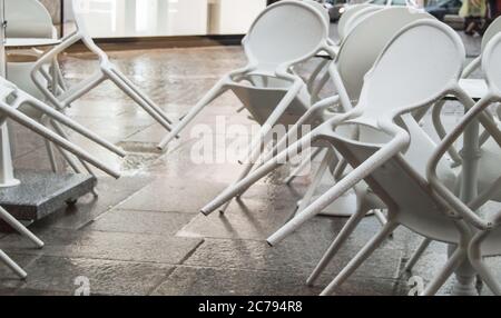 Chaises en plastique blanc humide avec gouttes de pluie dans un café de rue, renversé, après une pluie en Italie, dans la soirée. Banque D'Images