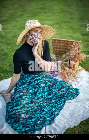 Belle jeune femme portant un masque facial coronavirus couvrant avec un motif floral pendant le verrouillage pandémique Covid-19 Banque D'Images