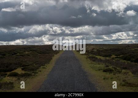 Cycliste solitaire dans la distance à parcourir vers le spectateur le long d'un sentier de moorland avec des nuages spectaculaires au-dessus Banque D'Images