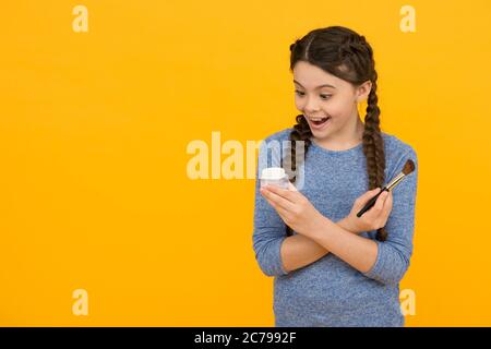 Aimez-vous plus. Concept de soin de la peau. Application de maquillage sur une peau saine. Produits de maquillage pour enfants. Espace de copie. studio de photo de fille faisant le maquillage. Surprise jeune fille faisant le maquillage à l'aide de brosse à poudre. Banque D'Images