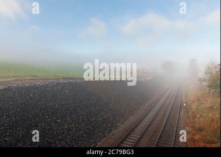 Piste ferroviaire en une coupure par un jour brumeux en Angleterre, au Royaume-Uni. Banque D'Images