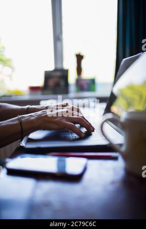 Mains d'une femme qui tape sur un ordinateur portable travaillant à domicile Banque D'Images