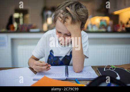 Un garçon concentré qui fait ses devoirs à table Banque D'Images